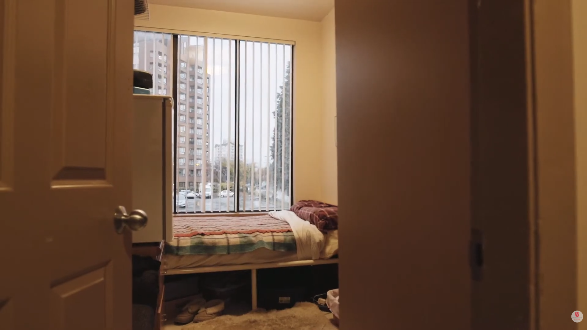 A private bedroom in the Genesis transitional housing program, showing a single bed and window in a safe, supportive living space.